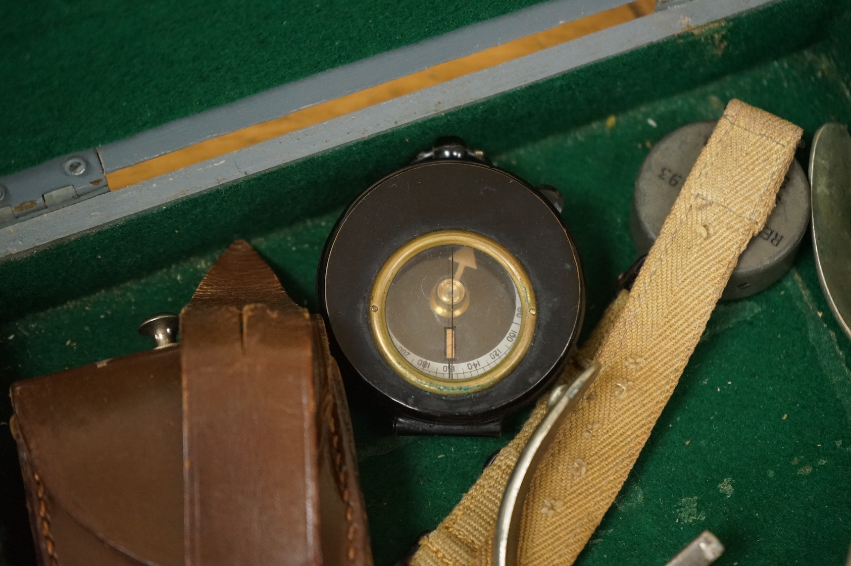 Three WWII military compasses including a Magnetic Marching Mark One compass, a small compass on a wrist strap and another in a leather case, together with a pair of steel spurs and a small grey painted wooden military b
